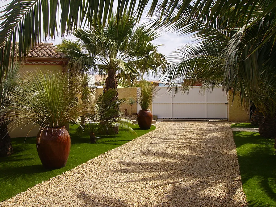 Entrata di una villa privata con il viale di ghiaia e il giardino con piante ed erba sintetica
