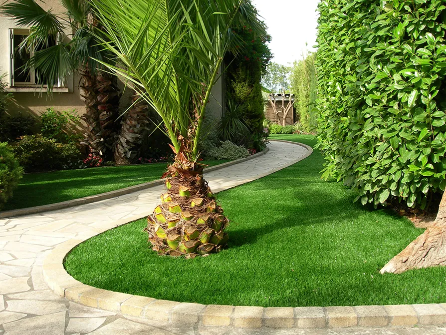 Giardino di una villa privata con erba sintetica attorniata da piante, vicino a un vialetto